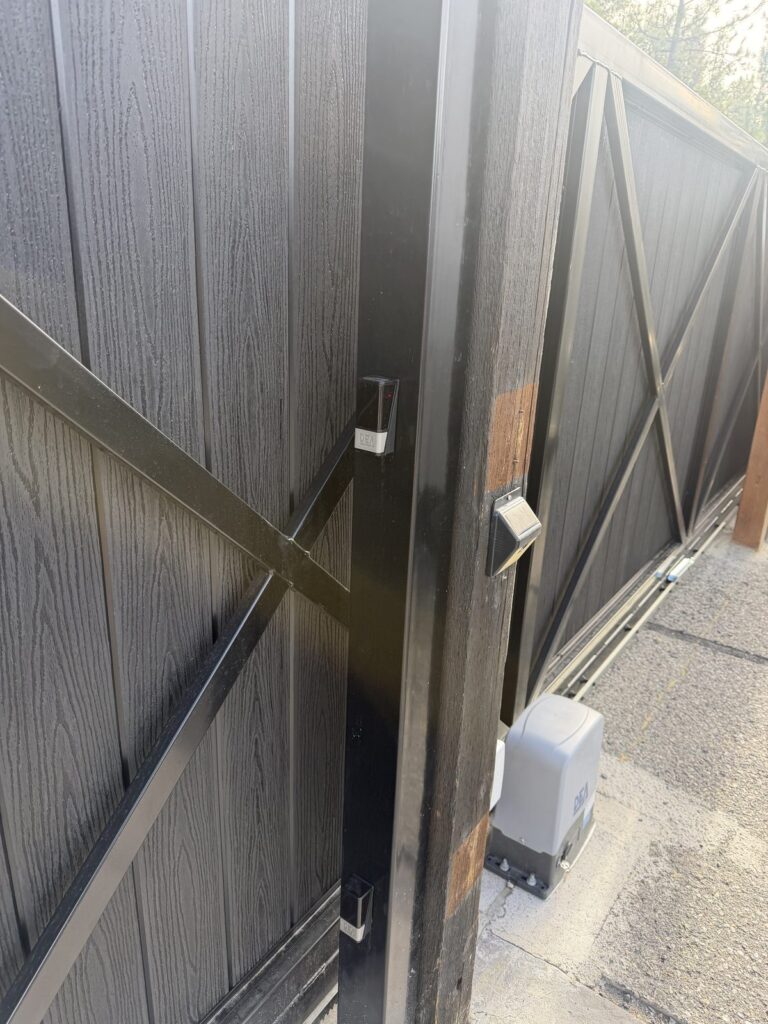 DEA photo eye mounted on a wood post beside a black composite gate with a lever latch